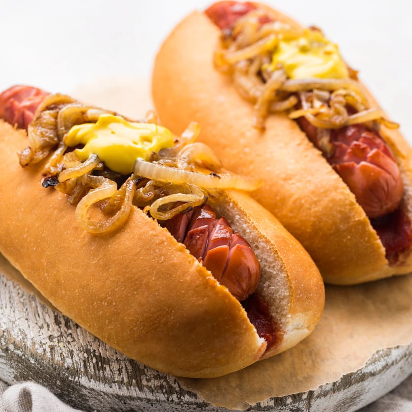 Two hot dogs with mustard and caramelized onions on a rustic wooden board.