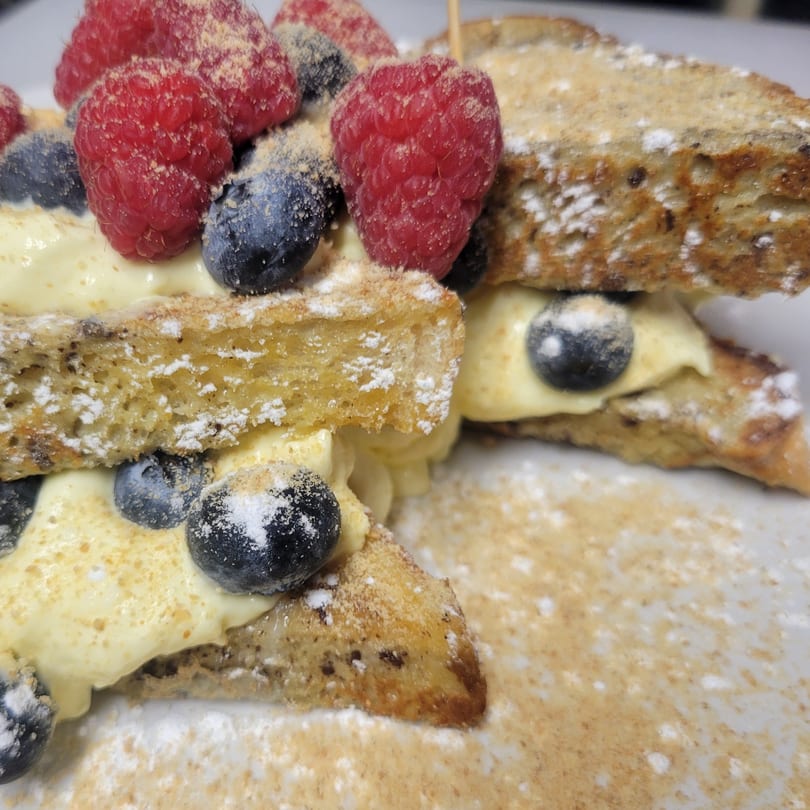 Close-up of French toast triangles with cream, raspberries, blueberries, and powdered sugar.