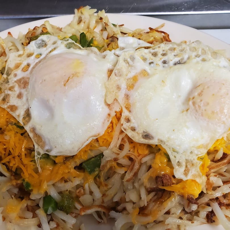 Two fried eggs with crispy edges sit atop a bed of hash browns, melted cheese, and green peppers.