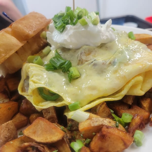 A close-up of a breakfast plate with an omelet, home fries, and toast.