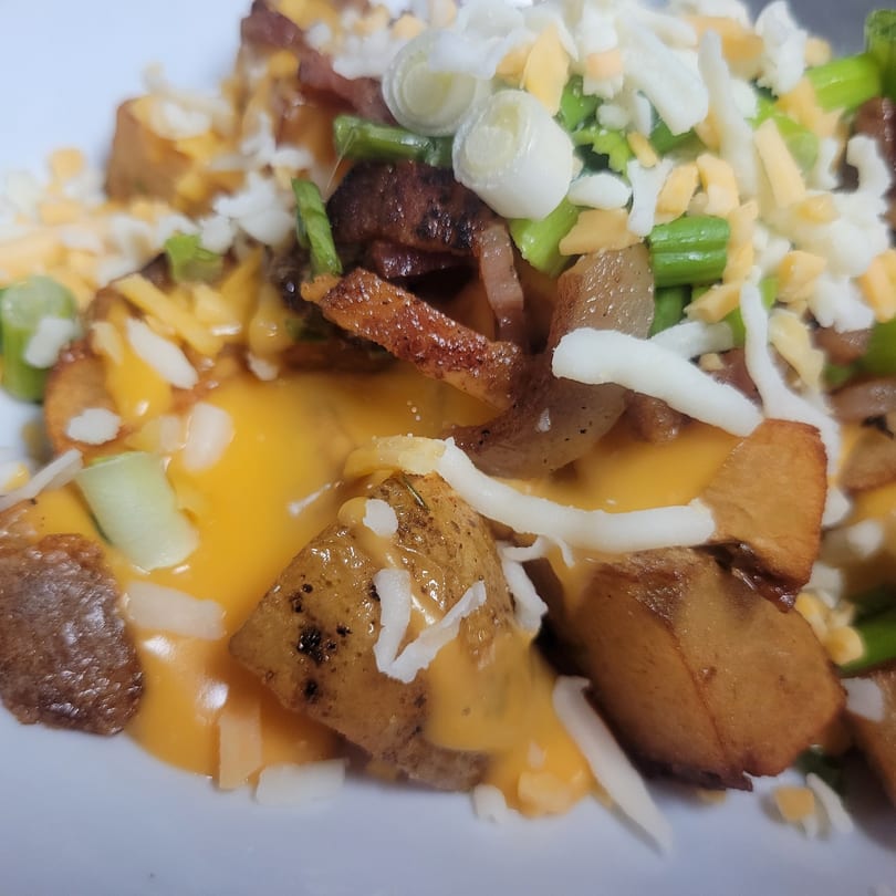 Close-up of golden-brown potato chunks covered in melted cheese, green onions, and white cheese crumbles.