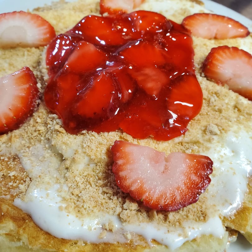 Close-up of a dessert with strawberry glaze, fresh strawberries, cream, and cookie crumbles.